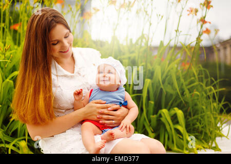 Cute smiling Toddler Baby sitting on Mom`s knees and having Fun. Relaxing in green summer Park. Selective focus. Image toned in Cute smiling Toddler Baby sitting on Mom`s knees and having Fun. Relaxing in green summer Park. Selective focus. Image toned in